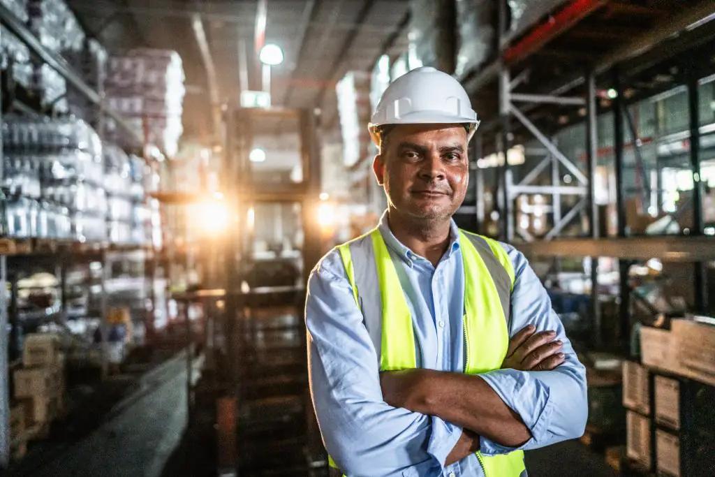 Homem vestindo EPI de braços cruzados em centro logístico. Homem vestindo EPI de braços cruzados em centro logístico.